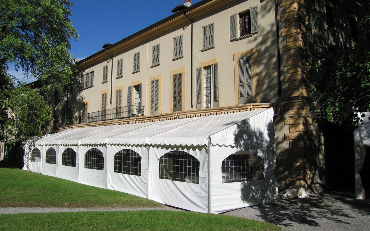 Tendostruttura monofalda con tamponamenti finestrati in pvc bianco addossata a facciata di villa storica per evento privato