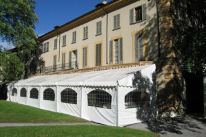 Tendostruttura monofalda con tamponamenti finestrati in pvc bianco addossata a facciata di villa storica per evento privato